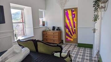 A bedroom with a bed, a dresser, a chandelier, a plaid-patterned floor, and a door with a colorful stained glass design.
