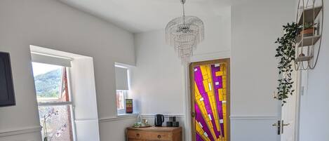 A bedroom with a bed, a dresser, a chandelier, a plaid-patterned floor, and a door with a colorful stained glass design.