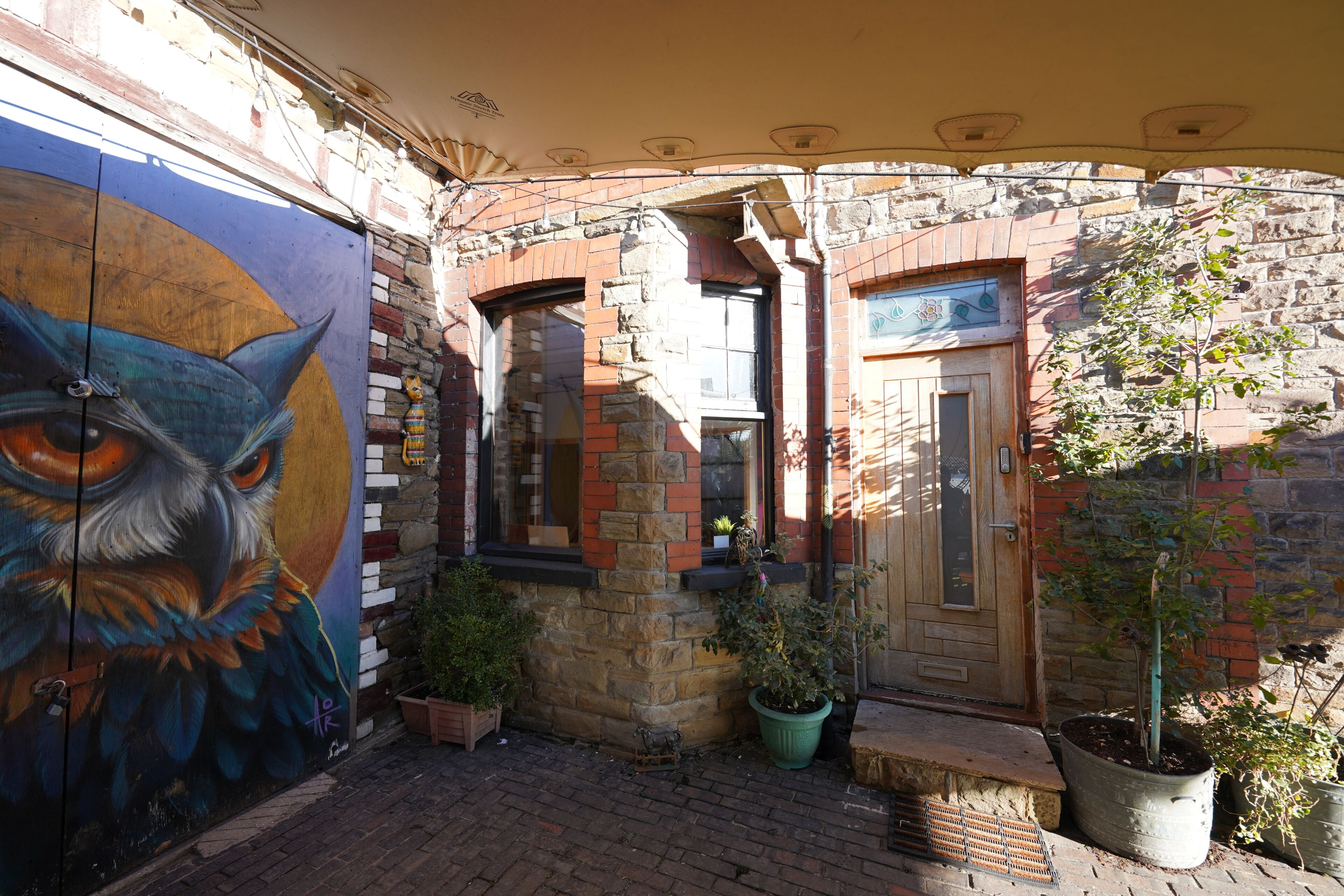 A courtyard with a mural, potted plants, and a brick building with a wooden door.