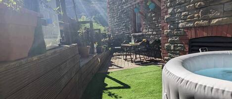 A stone building with a patio area, a hot tub, and a wooden fence.