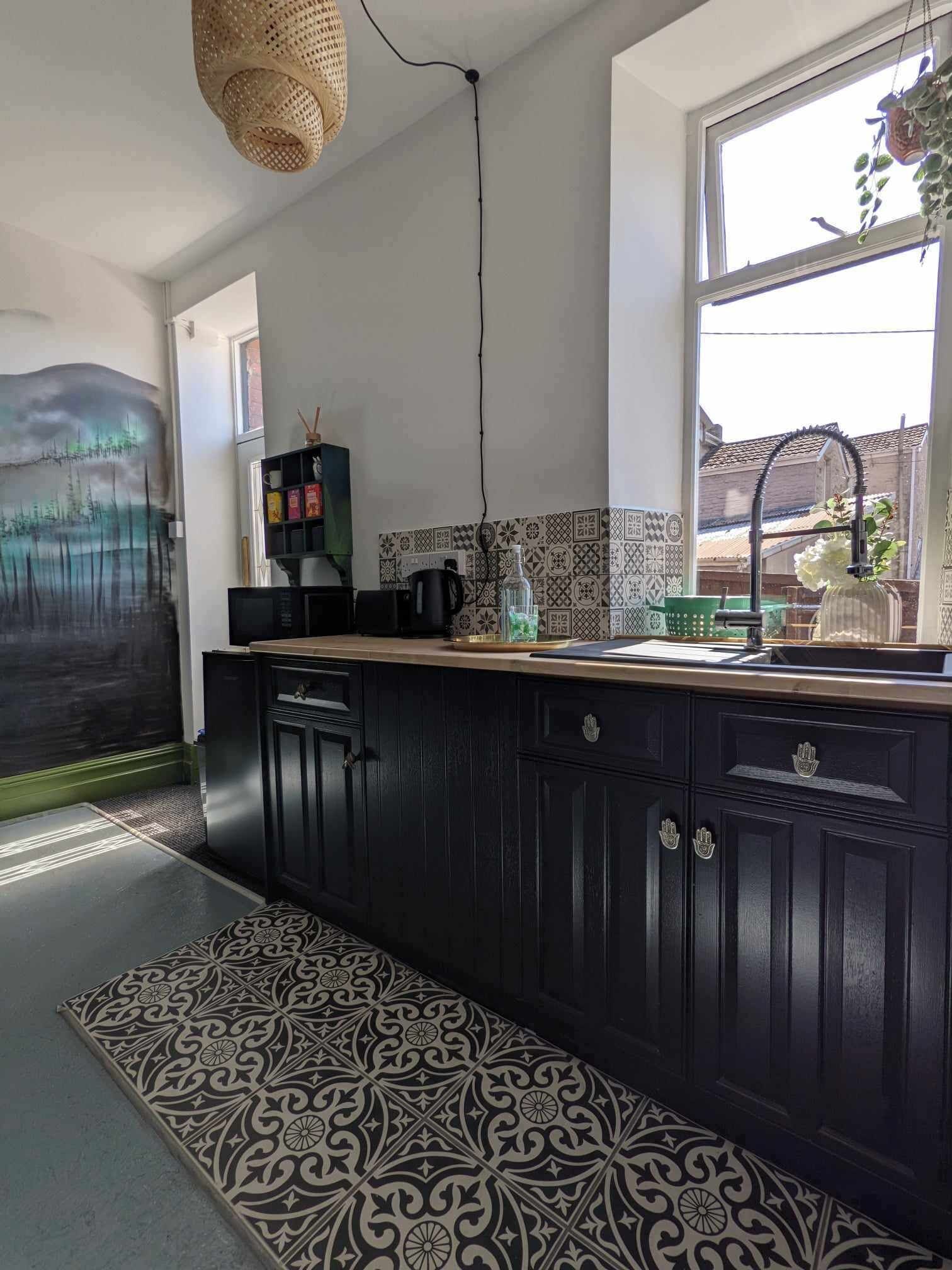 Una cocina con armarios de madera oscura, encimera negra y suelo estampado.