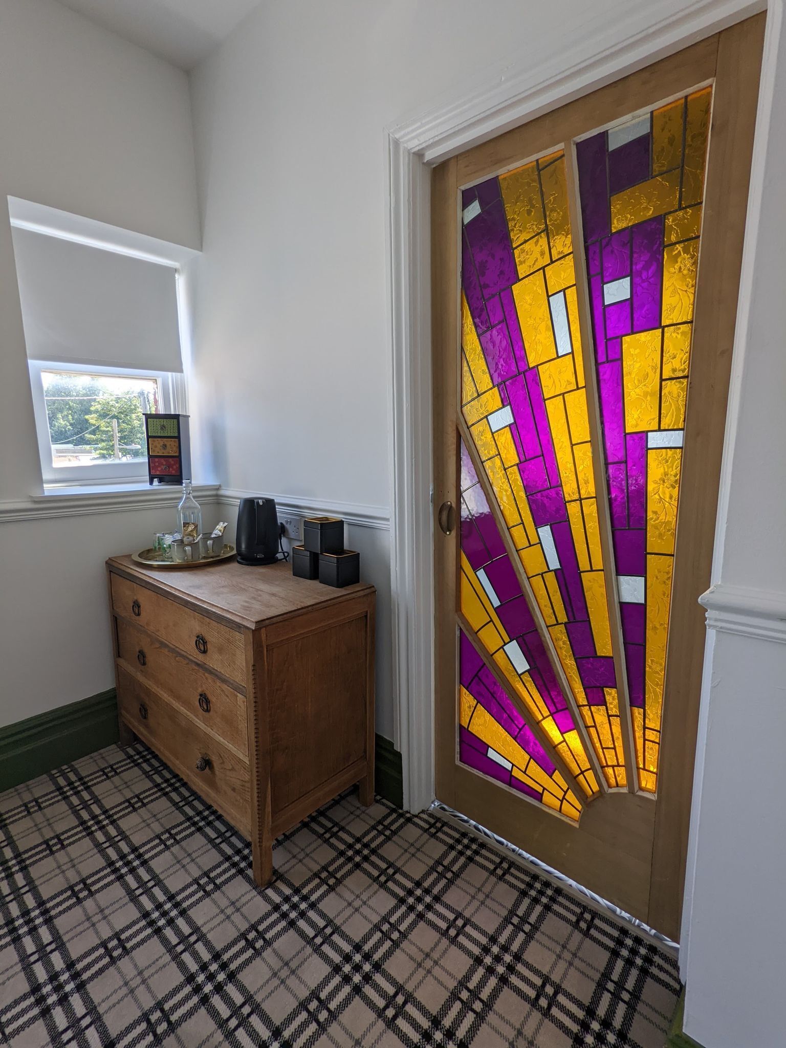 Quarto com piso xadrez, cômoda de madeira, janela e porta com vitrais.