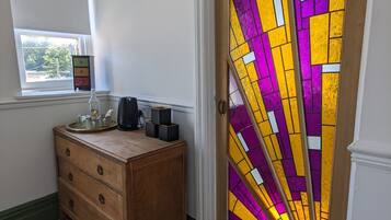 Quarto com piso xadrez, cômoda de madeira, janela e porta com vitrais.