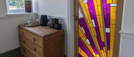 Quarto com piso xadrez, cômoda de madeira, janela e porta com vitrais.