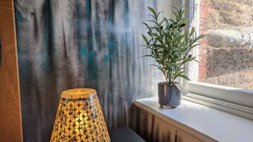 Una lámpara sobre una mesa negra, una planta en maceta en un alféizar y una pared con estampado de bosque.