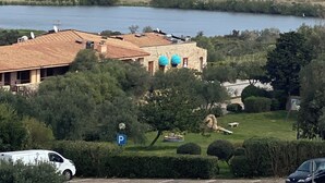 Vista sulla costa con un edificio dotato di tetto in tegole e antenne paraboliche, un segnale di parcheggio e un corpo d'acqua.