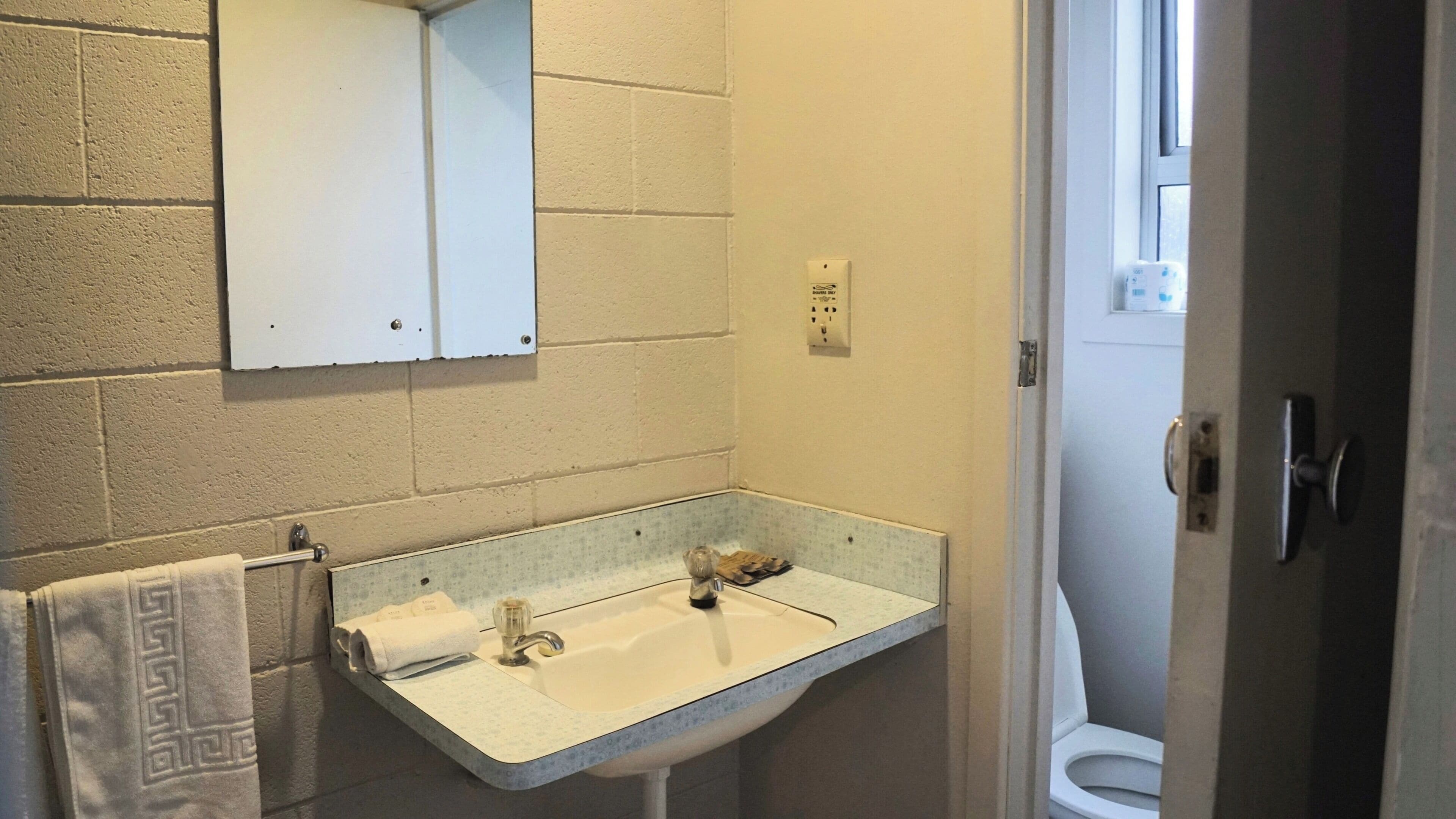 A bathroom with a white sink, a towel rack with a patterned towel, a mirror, and a toilet visible through an open door.