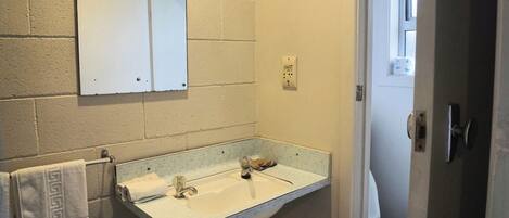 A bathroom with a white sink, a towel rack with a patterned towel, a mirror, and a toilet visible through an open door.