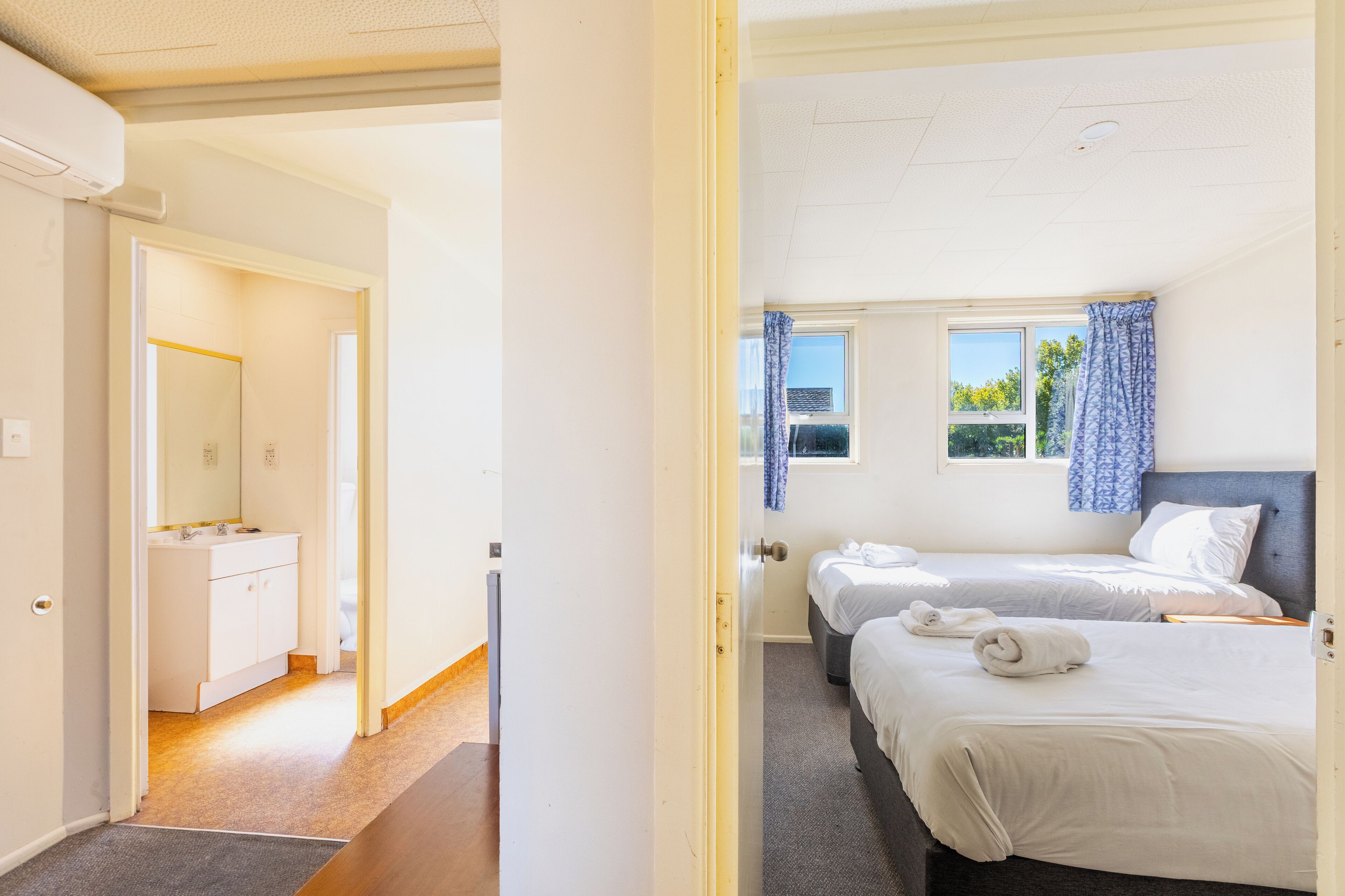 A hotel room with two beds, a bathroom with a sink, and a window with curtains.