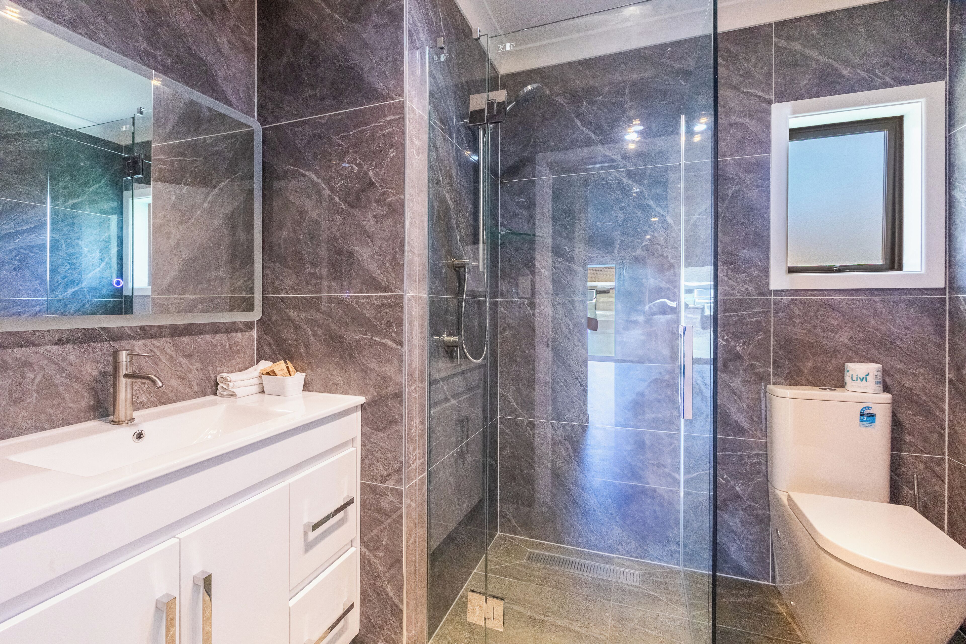 A modern bathroom with a glass-enclosed shower, a white sink, and a toilet.