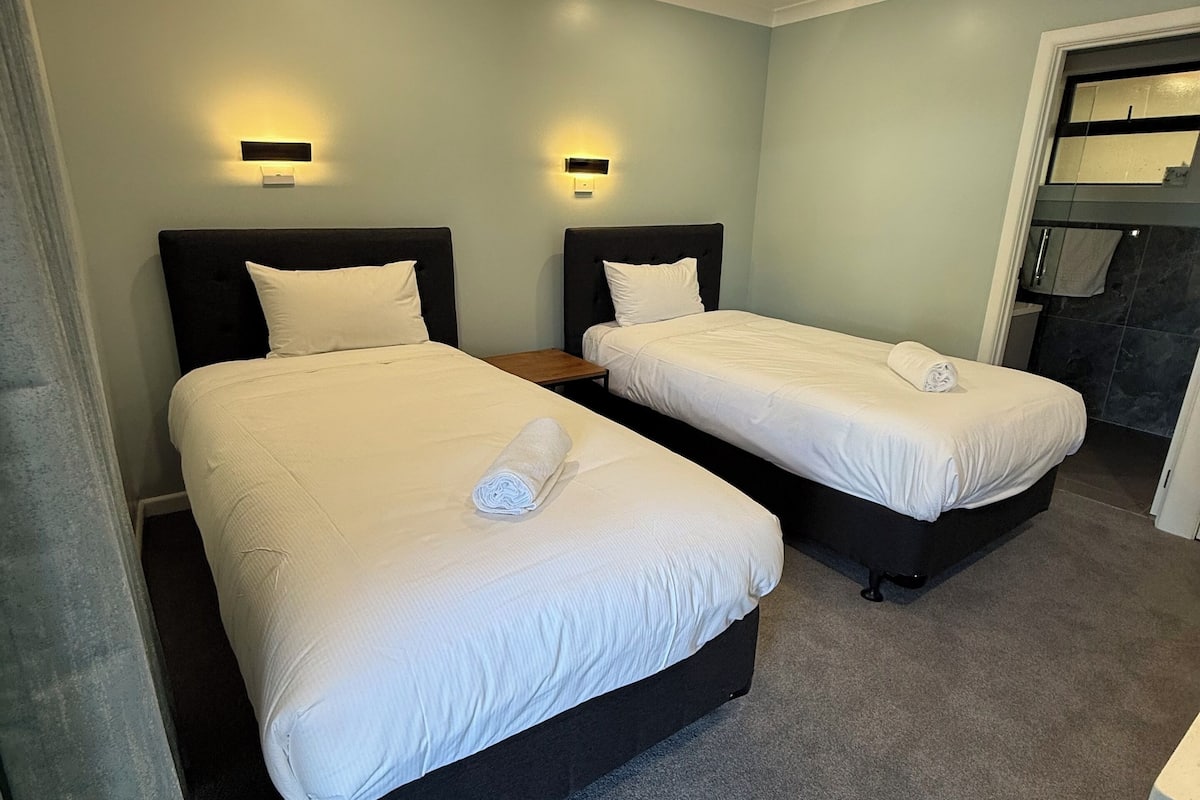 A hotel room with two beds, each with a headboard and a bedside table.