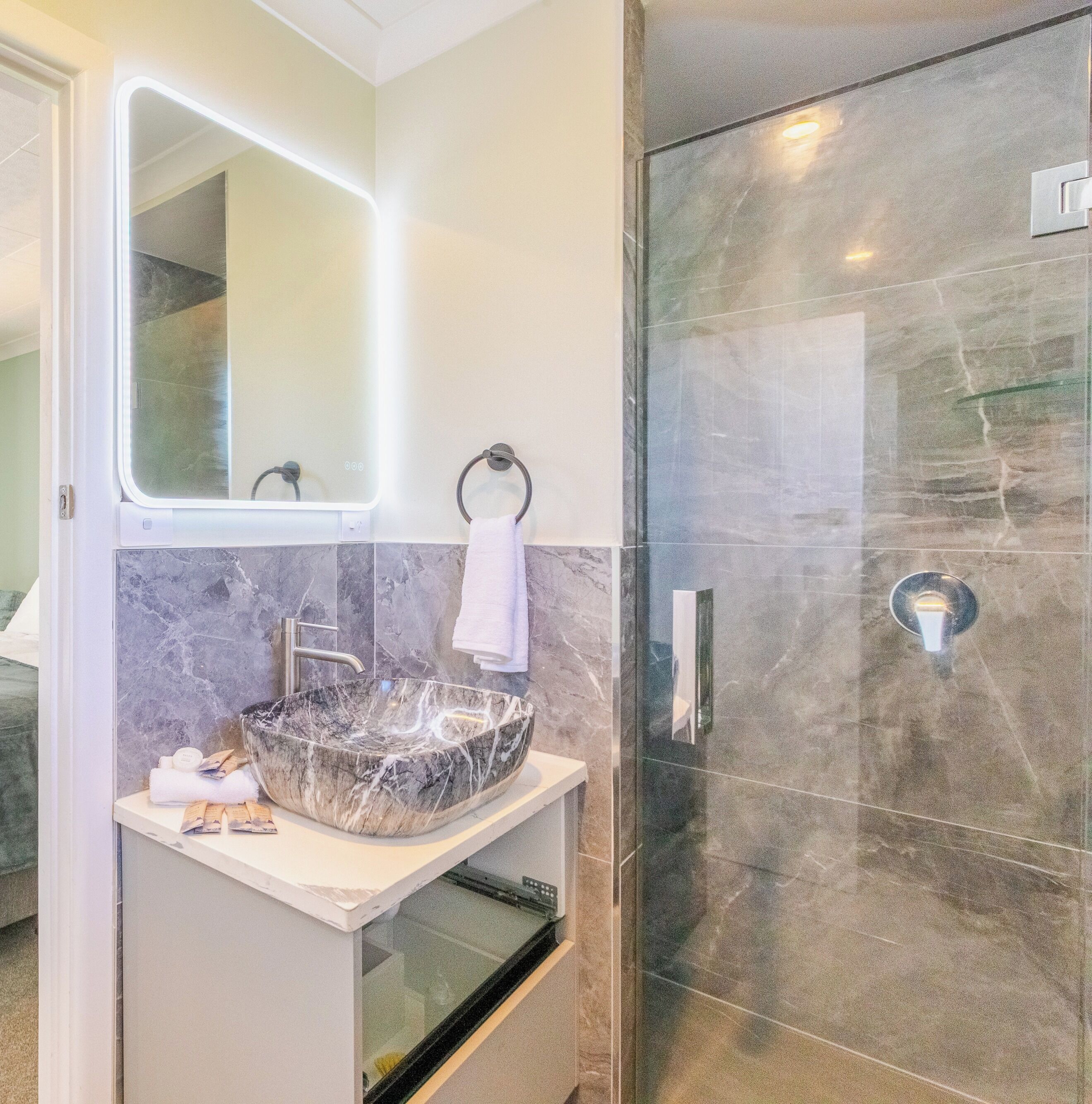 Une salle de bain moderne avec un lavabo en marbre, une douche à parois de verre et un miroir fixé au mur.