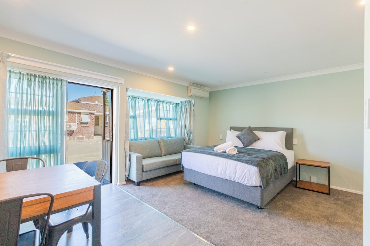 A bedroom with a bed, a sofa, a table, and a small side table.