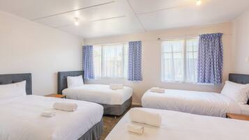 Habitación de hotel con tres camas, cada una con ropa de cama y toallas blancas, un ventilador de techo y ventanas con cortinas azules.