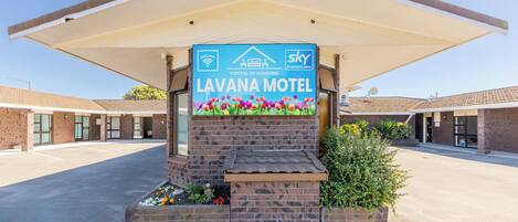 Un motel con un cartel que anuncia Wi-Fi gratuito y Sky TV, rodeado de un estacionamiento y un pasillo cubierto.