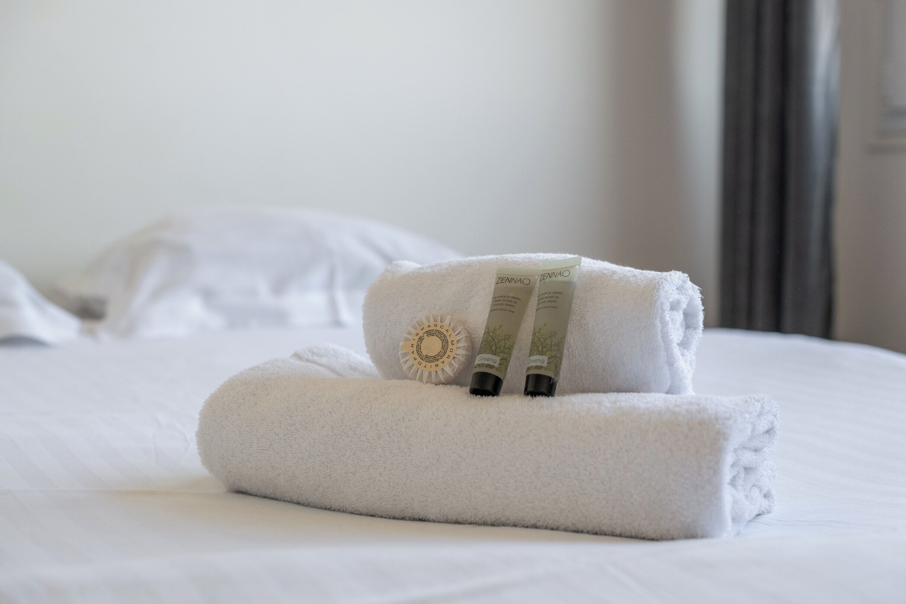 A neatly made bed with two rolled towels and two bottles of lotion.