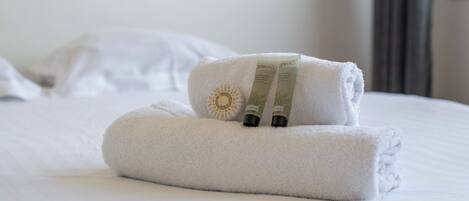 A neatly made bed with two rolled towels and two bottles of lotion.