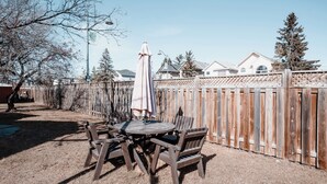 A backyard with a wooden fence, a round table with chairs, and an umbrella. - The Cloud off 16th  (Calgary)