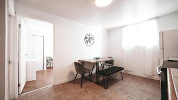 A room with a dining table, chairs, a bench, a piano, and a wall clock.