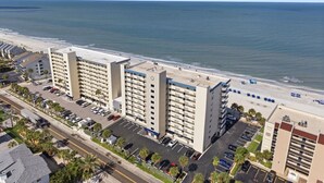 A multi-story hotel with a parking lot, located near a beach with the ocean in the background. - Beachfront 3 bedroom with Amazing Views! (Indian Shores)