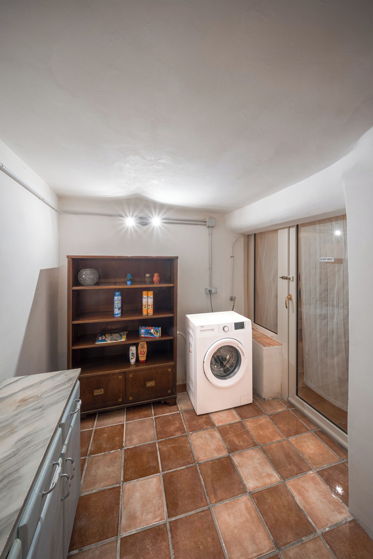 A laundry room with a washing machine, a wooden cabinet with various items, and a 'Staff Only' door.