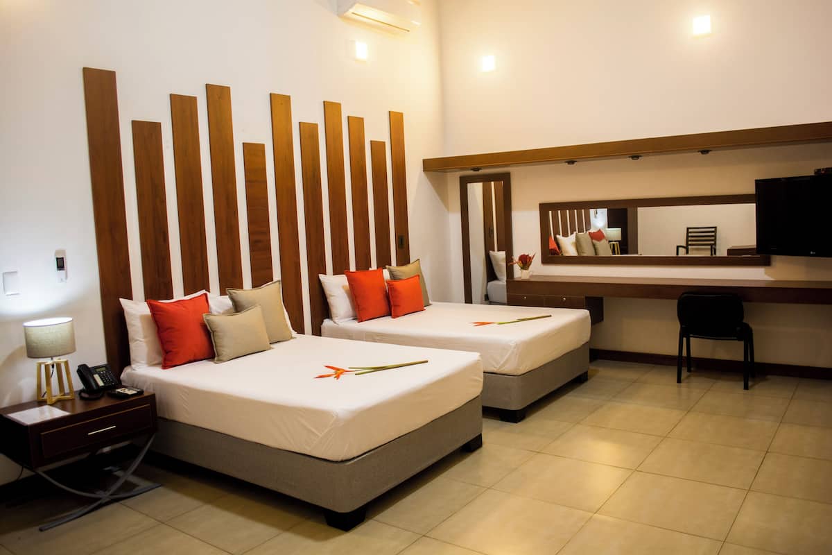 Quarto de hotel com duas camas, uma escrivaninha, uma cadeira, uma televisão e um espelho.