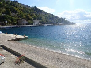 A coastal area with a pebbled beach, a pier, and buildings on a hillside. - Holiday apartment with sea view (Barić Draga)