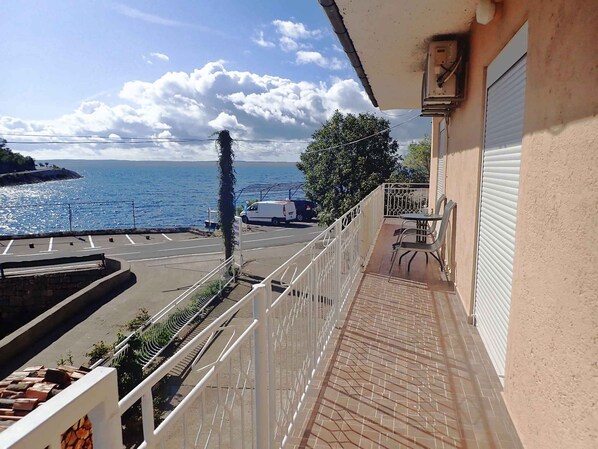 A balcony with a view of the sea, a parked van, and a building with a closed shutter. - Holiday apartment with sea view (Barić Draga)