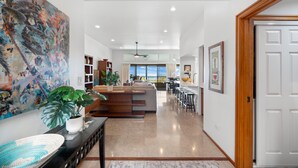 A spacious living area with a large painting, a dining area, and a kitchen. - Kapalua Ridge Villas 1023 (Lahaina)