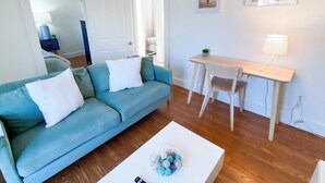Een moderne woonkamer met een blauwgroene bank, een witte salontafel en een houten bureau met een stoel.