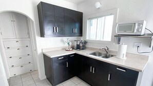 Een moderne keuken met zwarte kastjes, een wit aanrecht, een dubbele spoelbak, een magnetron en een raam met jaloezieën.