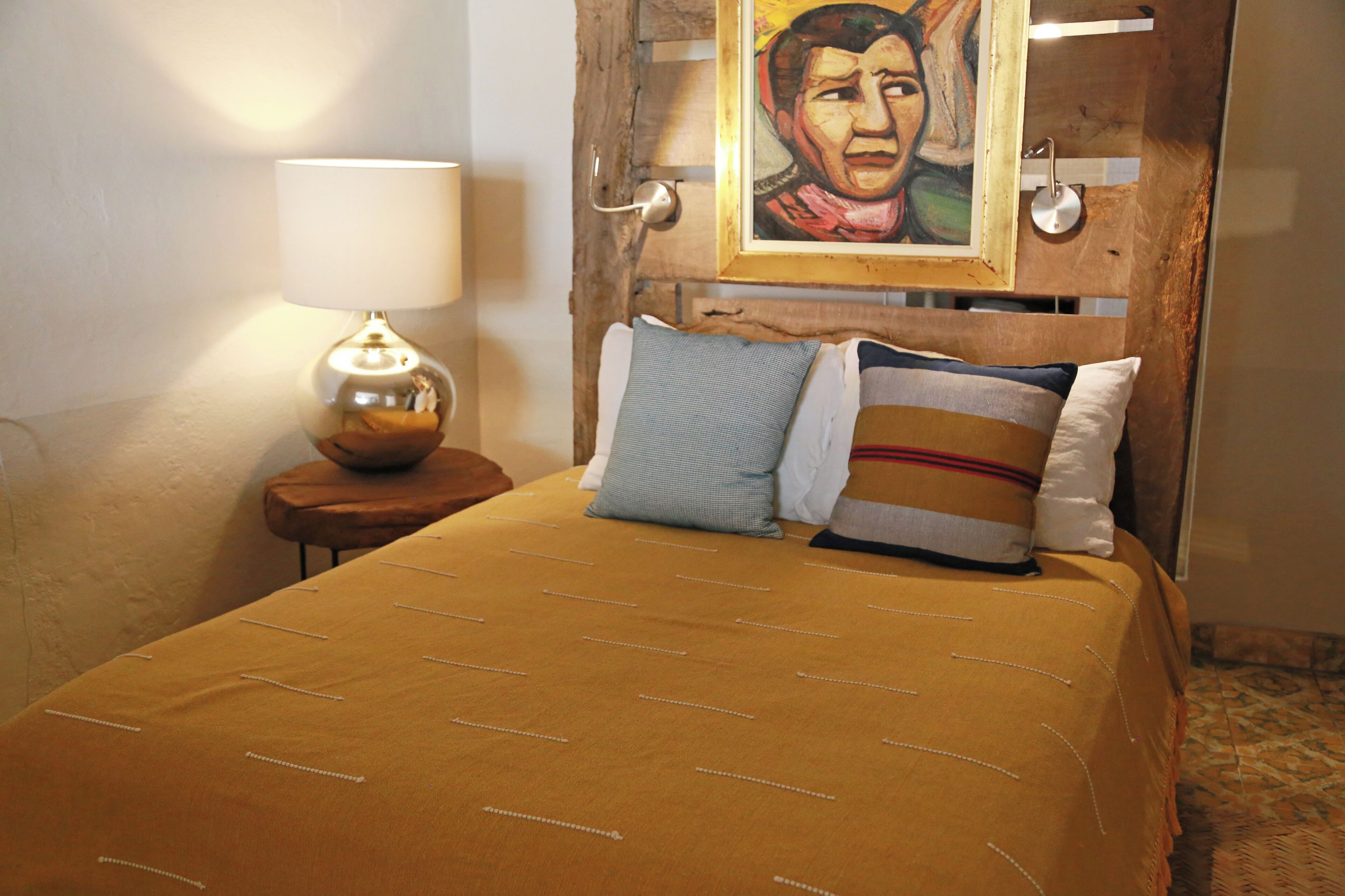 A bed with a brown bedspread and two pillows, a nightstand with a lamp, and a painting on the wall.
