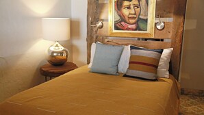 A bed with a brown bedspread and two pillows, a nightstand with a lamp, and a painting on the wall. - Cazules #2 (Puerto Vallarta)