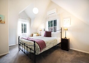 Un dormitorio con una cama, dos mesitas de noche, un ventanal y un equipo de aire acondicionado.