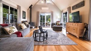 A spacious living room with a high ceiling, a fireplace, a television, and a large window offering a view of the outdoors.
