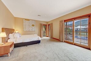 Ein geräumiges Schlafzimmer mit einem großen Bett, einem Nachttisch, einer Wanddekoration und einer Glasschiebetür, die auf einen Balkon führt.