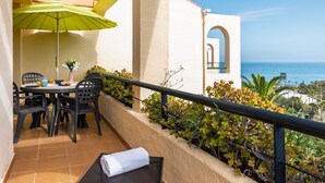 A balcony with a table and chairs, a green umbrella, and a view of the sea.