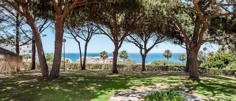 Ein angelegter Garten mit alten Bäumen, einem Kiesweg und Blick auf das Meer.