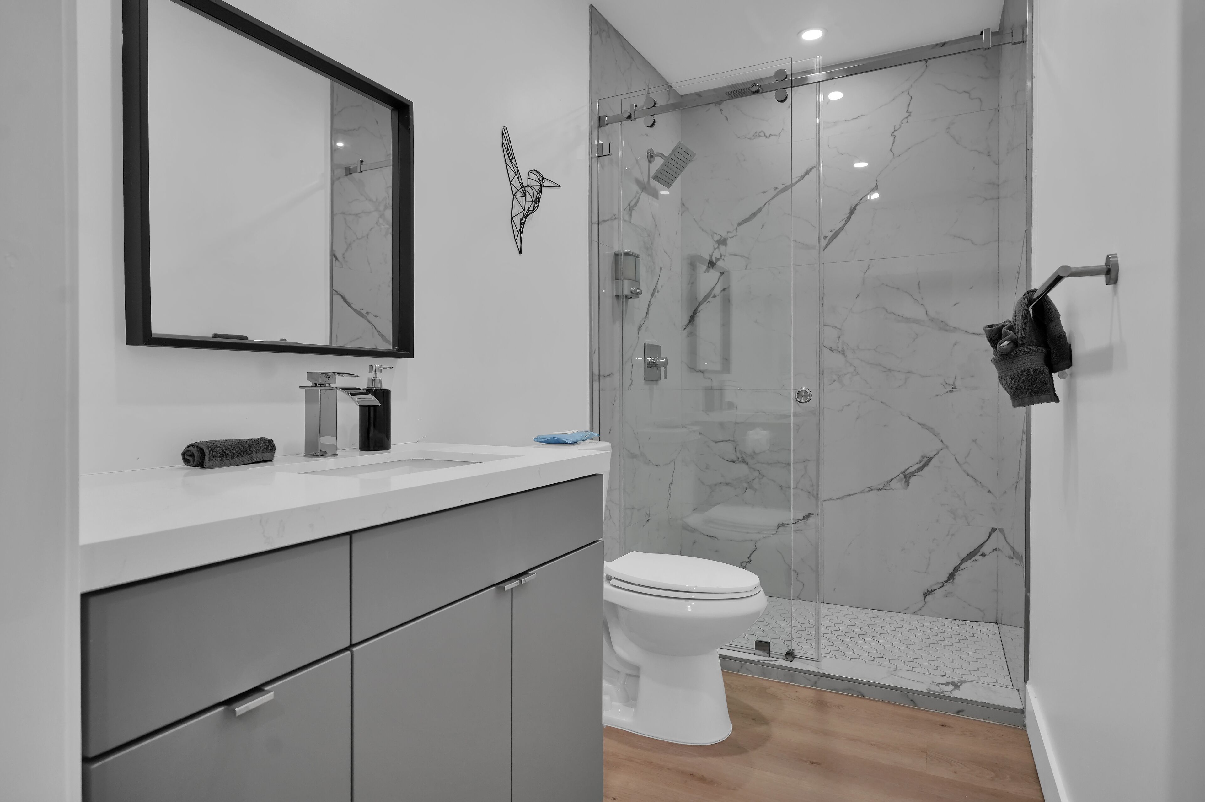 Ein modernes Badezimmer mit einer Marmordusche, einer Toilette und einem Waschbecken mit Spiegel darüber.