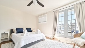 Une chambre à coucher comprenant un lit, des tables de chevet, une chaise, un balcon avec des rideaux et un ventilateur de plafond.