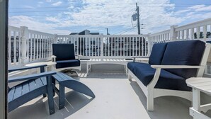 Un espace extérieur abrité, avec des rampes blanches, deux chaises bleu foncé et une petite table.