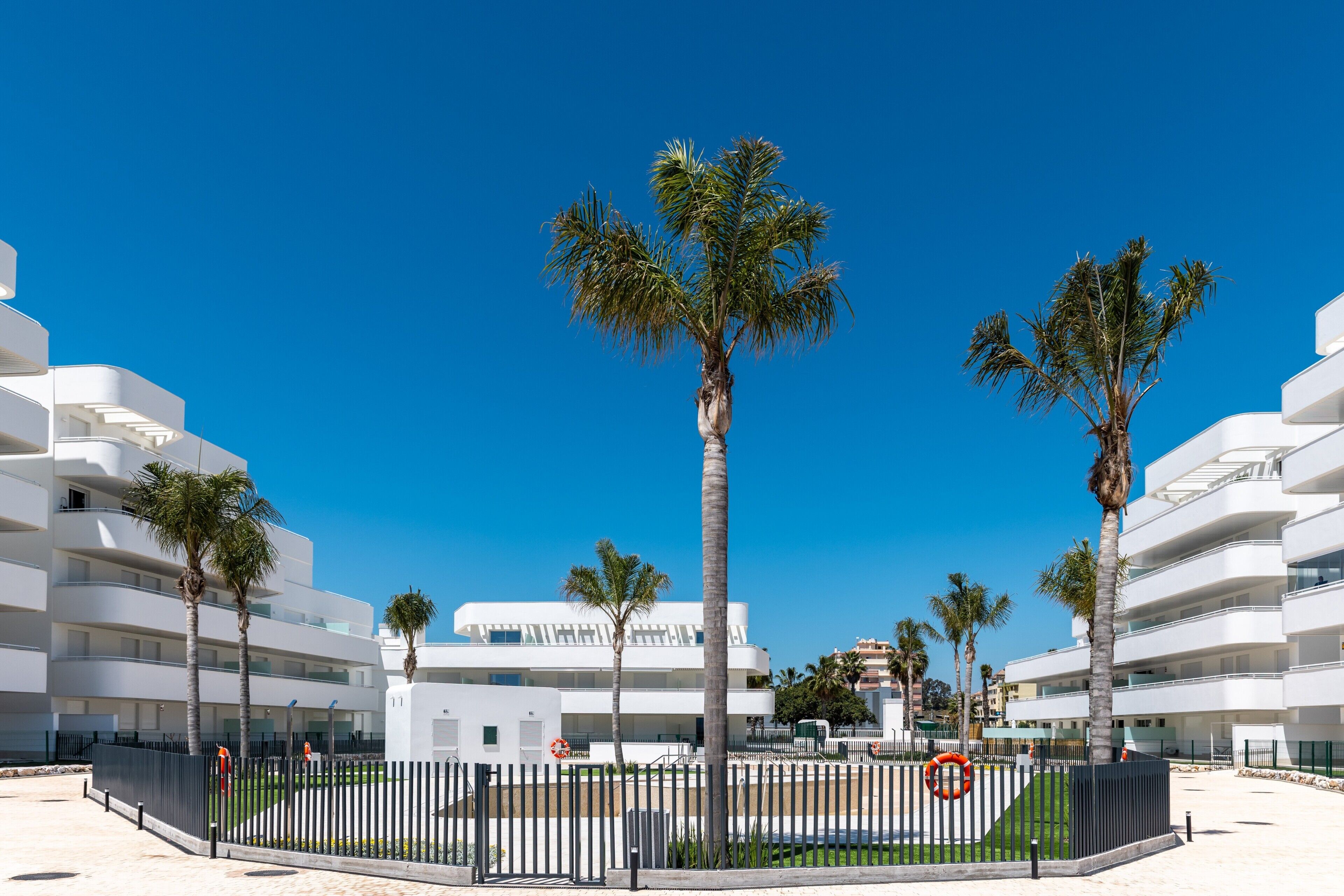 Ein modernes Hotel mit mehreren Stockwerken, Palmen und blauem Himmel.