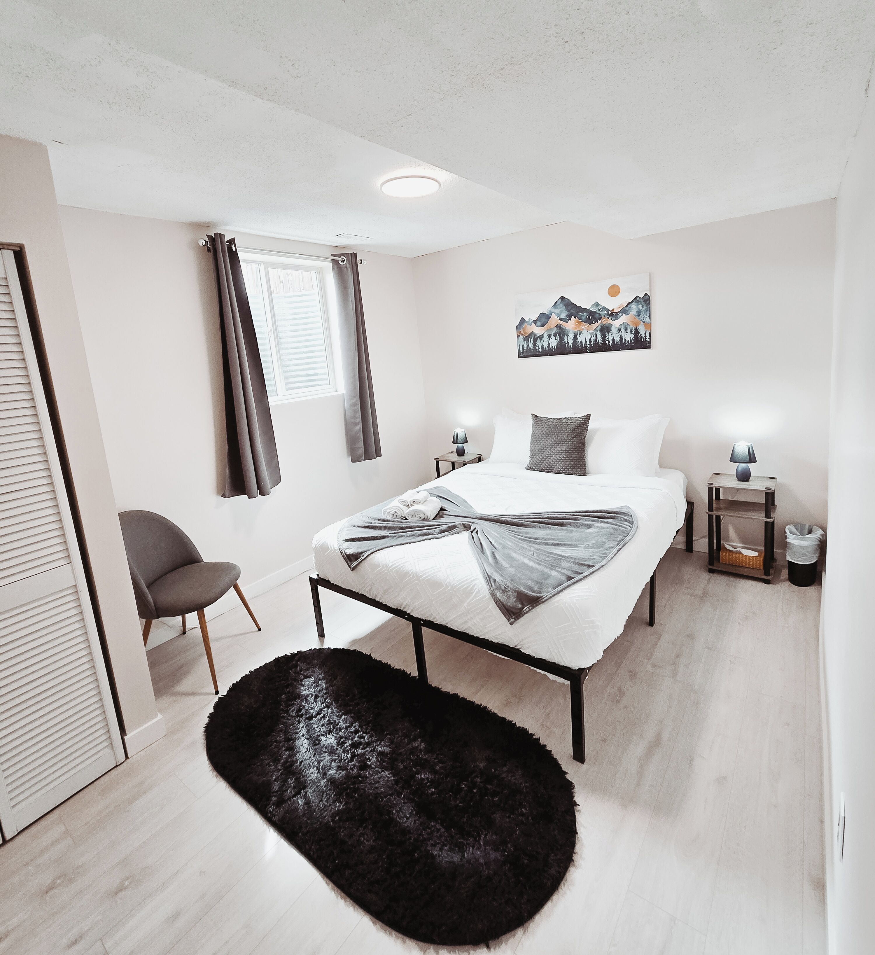 A modern bedroom with a bed, a chair, a black furry rug, a painting, and a window with curtains.