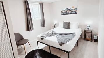 A modern bedroom with a bed, a chair, a black furry rug, a painting, and a window with curtains.