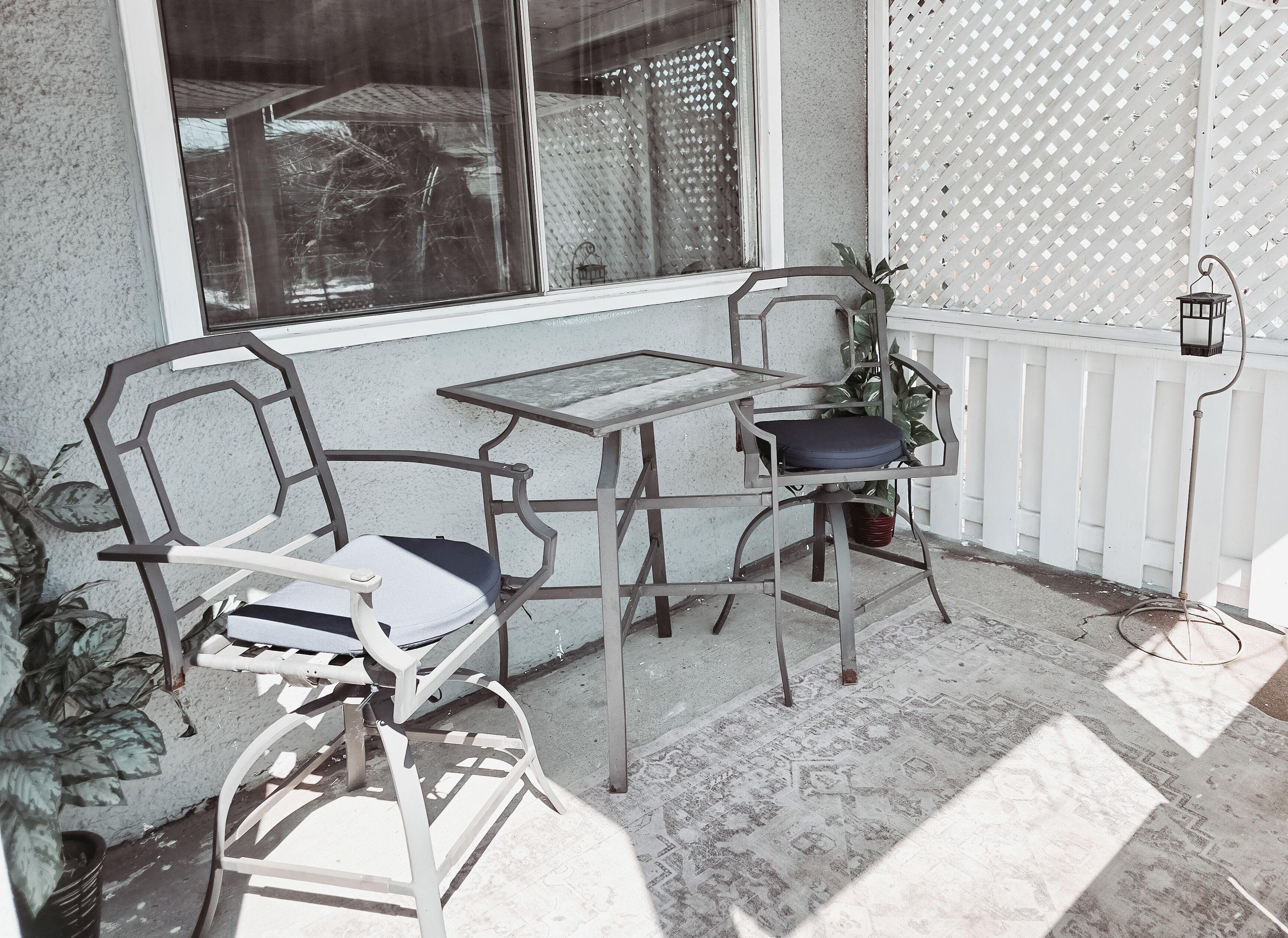 Un patio con una mesa, dos sillas, una planta en maceta y una valla blanca.