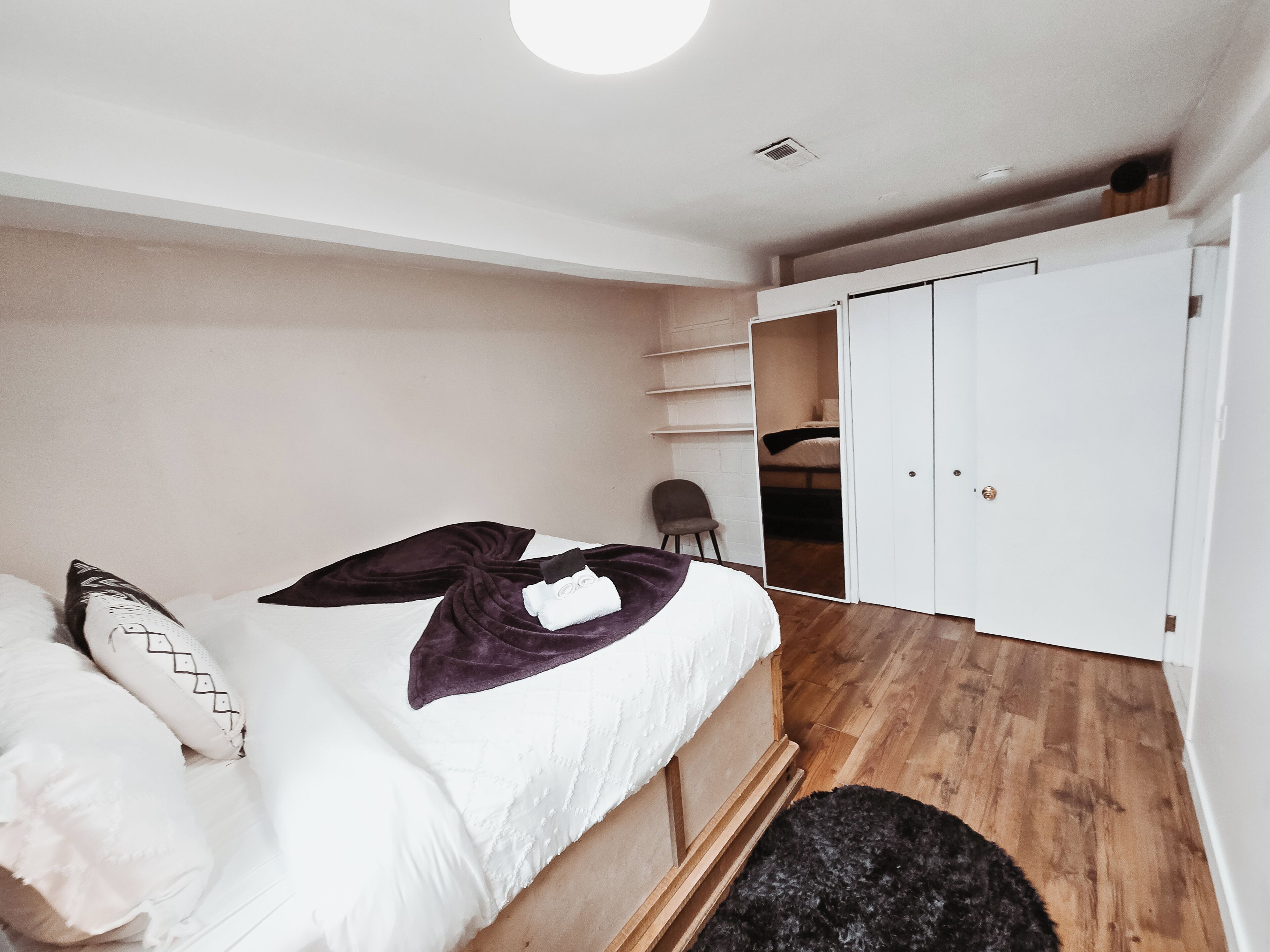 A bedroom with a bed, a chair, a wardrobe, and a small closet.