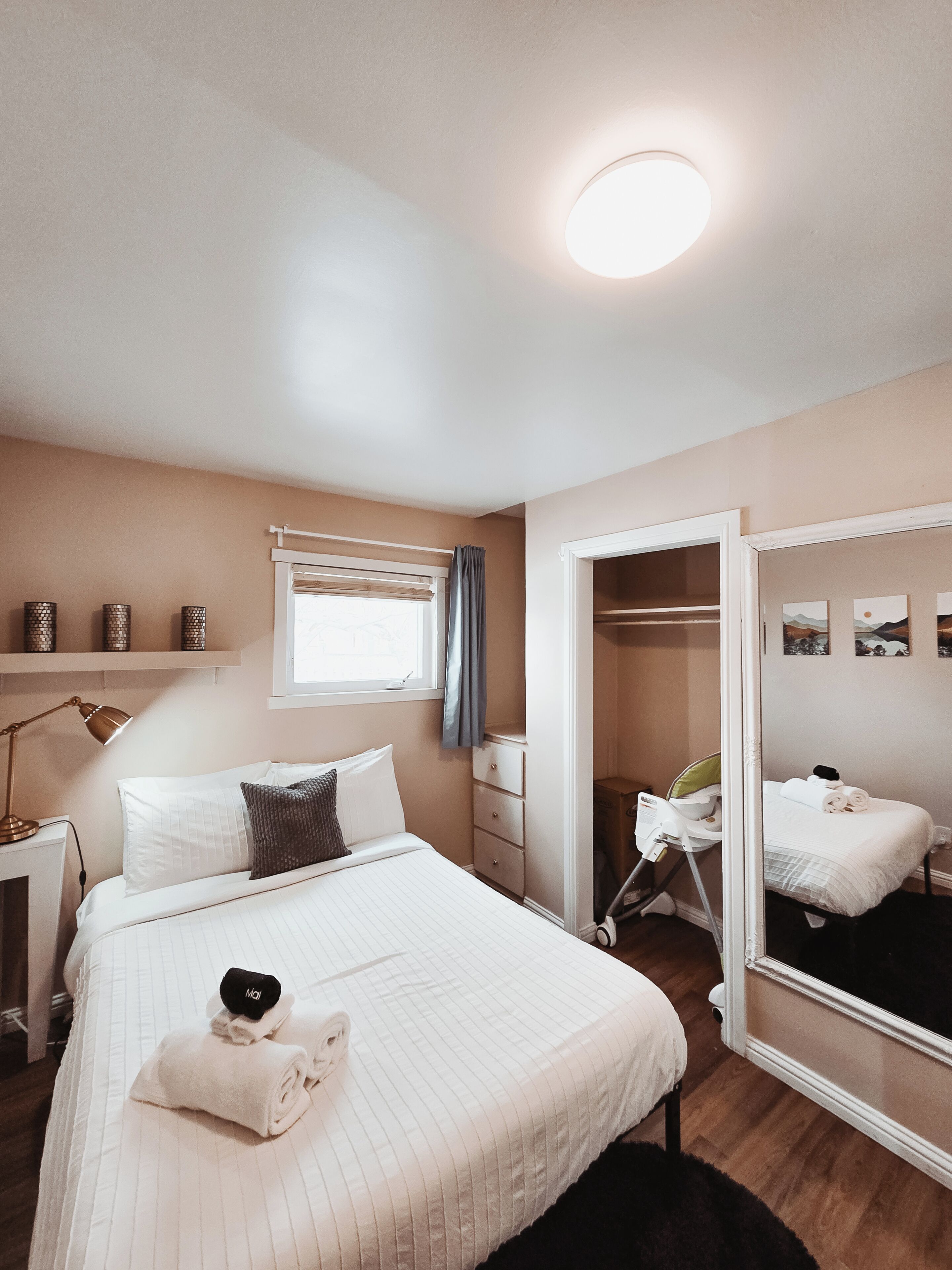 A bedroom with a bed, bedside lamp, dresser, and a large mirror.