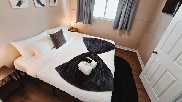 Habitación de hotel con cama, una obra de arte en la pared, una mesita de noche con lámpara y una ventana con cortinas.
