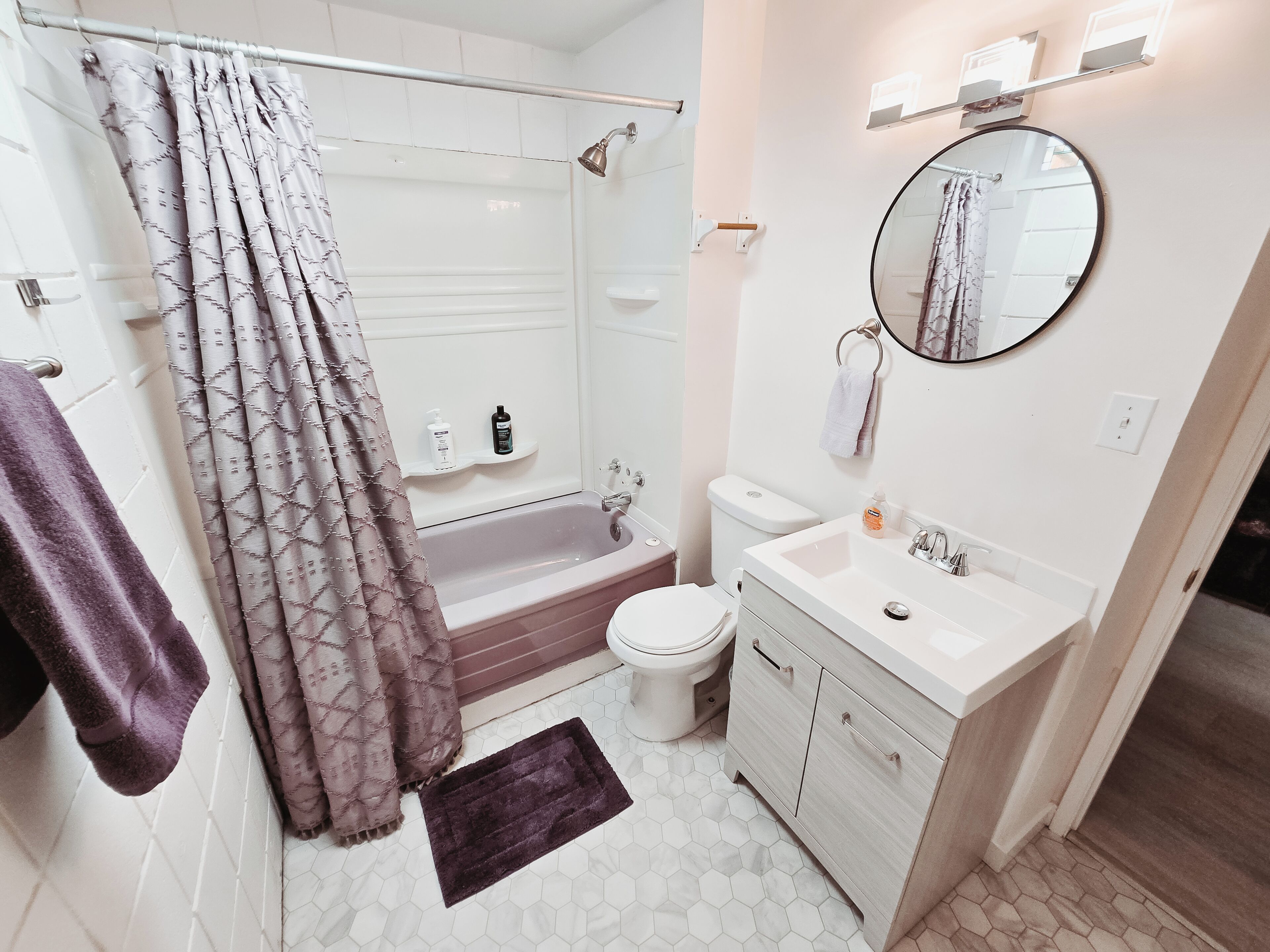 A bathroom with a shower, toilet, sink, and a mirror.