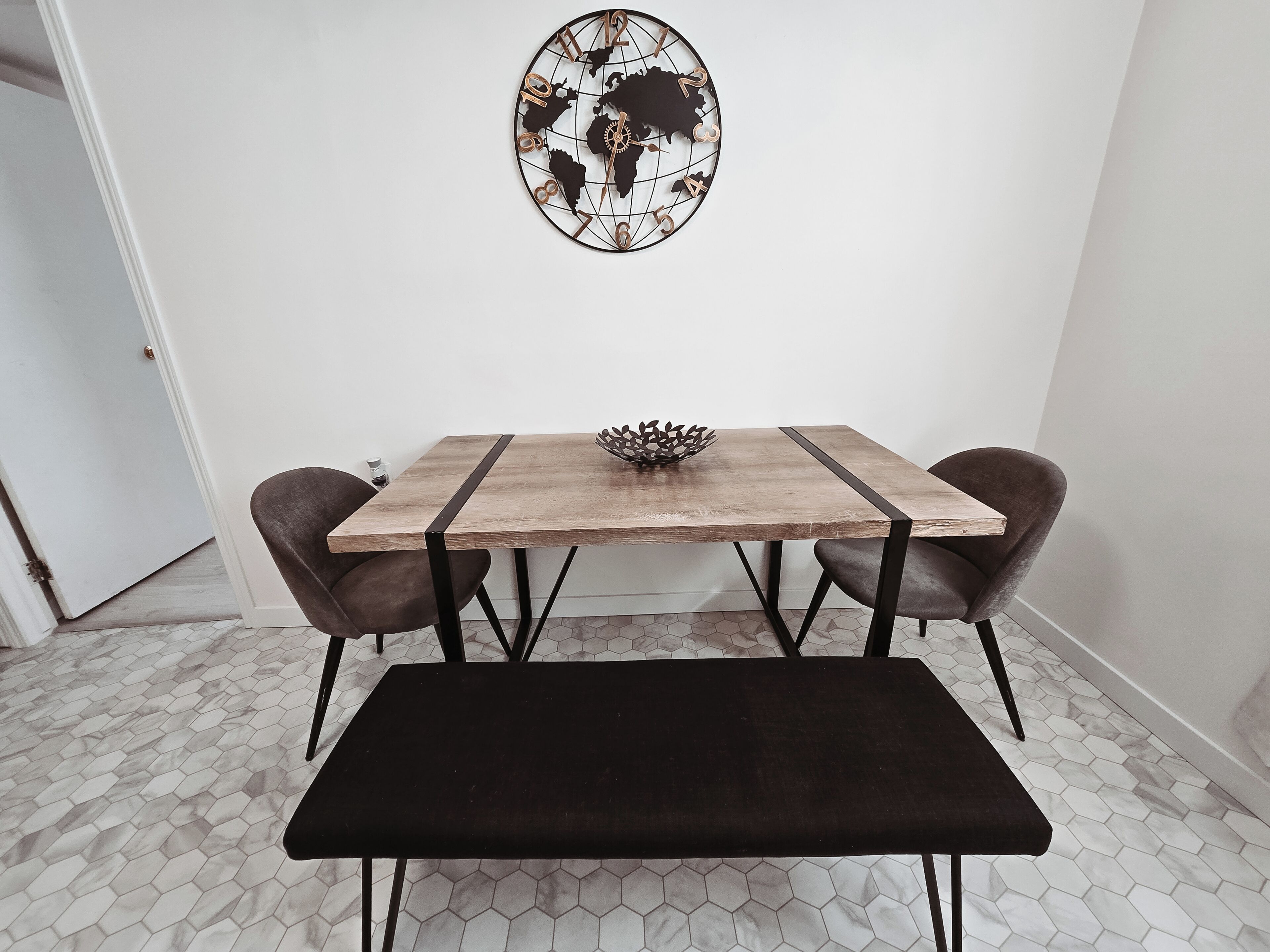 Een eethoek met een houten tafel, twee stoelen, een bank en een decoratief object aan de muur.